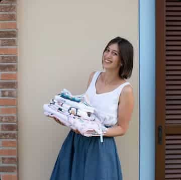 Chiara con i bavaglini e altri articoli per l'infanzia di Bavarin Chiara di Bavarin che regge in mano i bavaglini e altri articoli per l'infanzia fatti a mano da lei